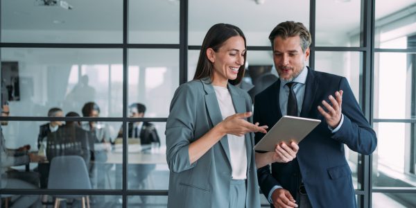 Shot of two coworkers having a discussion in modern office. Businessman and businesswoman in meeting using digital tablet and discussing business strategy. Confident business people working together in the office. Corporate business persons discussing new project and sharing ideas in the workplace.
